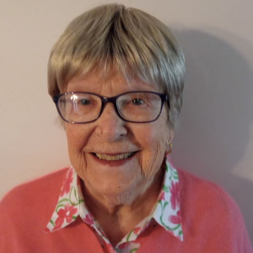 A woman with glasses and short hair wearing a pink shirt.