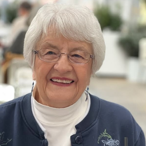 A woman with white hair and glasses smiling.