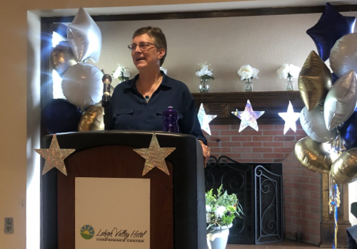 A woman standing at the podium with a cat on her lap.