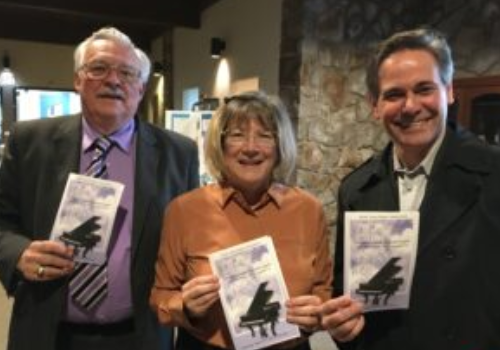 Three people holding up books in front of a wall.