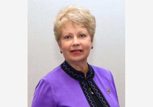 A woman in purple shirt and black tie.